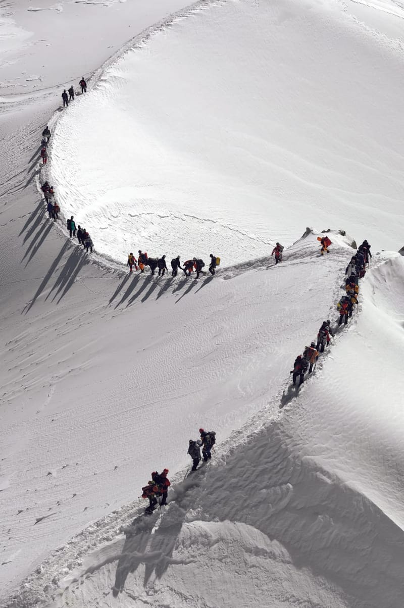 A team of climbers moving in single file along a snowy ridge — coordinated, together.